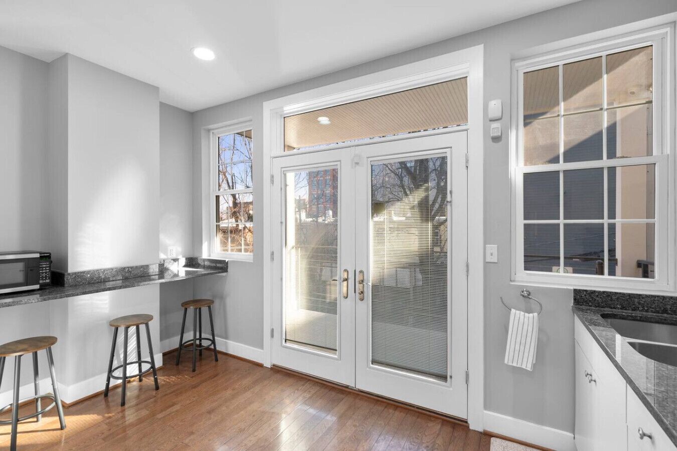 A kitchen with a microwave, two stools, a large sliding glass door, and a window.