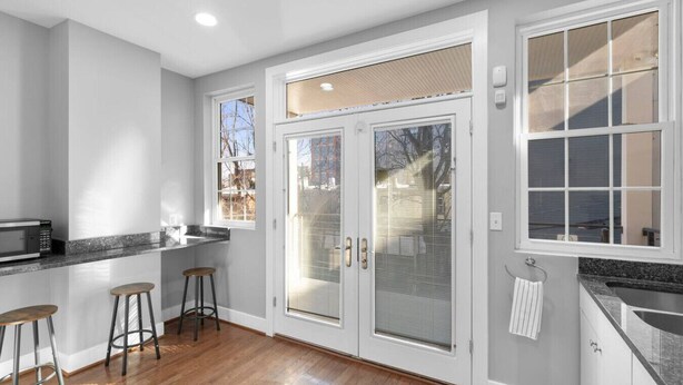 A kitchen with a microwave, two stools, a large sliding glass door, and a window.