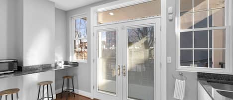 A kitchen with a microwave, two stools, a large sliding glass door, and a window.