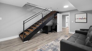 A modern living room with a wooden staircase, a gray couch, and a cityscape painting on the wall.