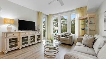 Una sala de estar con televisión, una mesa de centro de vidrio, un sofá, un mueble y un ventilador de techo.