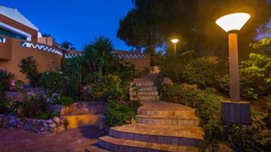 A nighttime outdoor staircase with a lamp post, surrounded by greenery and a building with zigzag patterns. - 1-Bedroom Apartment with Pool and Garden View (3 Adults) (Luz)