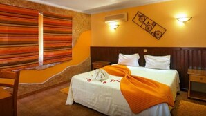 A hotel room with a bed, a nightstand, a chair, a wall with a striped pattern, and a wall-mounted air conditioner. - 1-Bedroom Apartment with Pool and Garden View (3 Adults) (Luz)