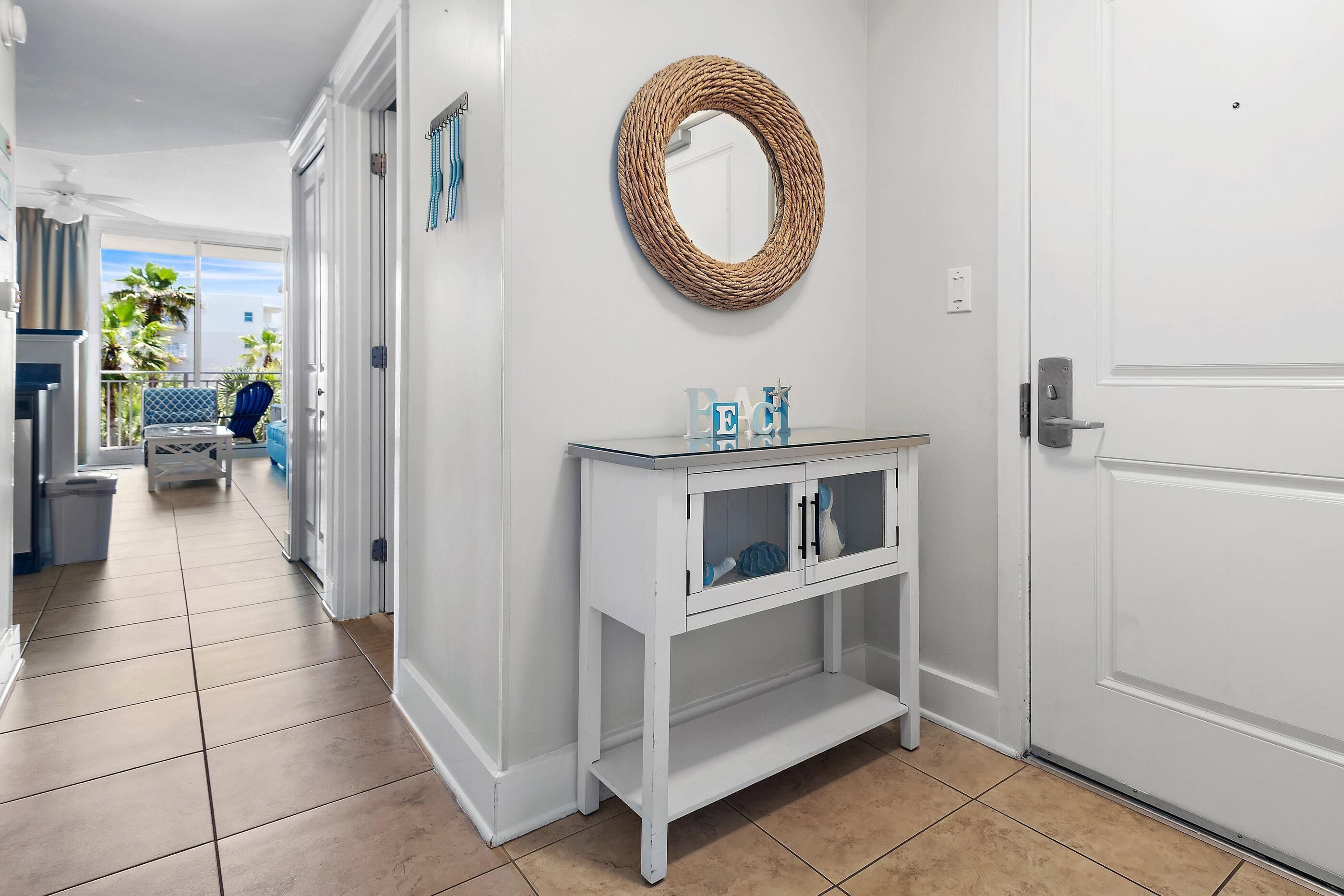 A hallway with a white console table, a woven mirror, and a door.