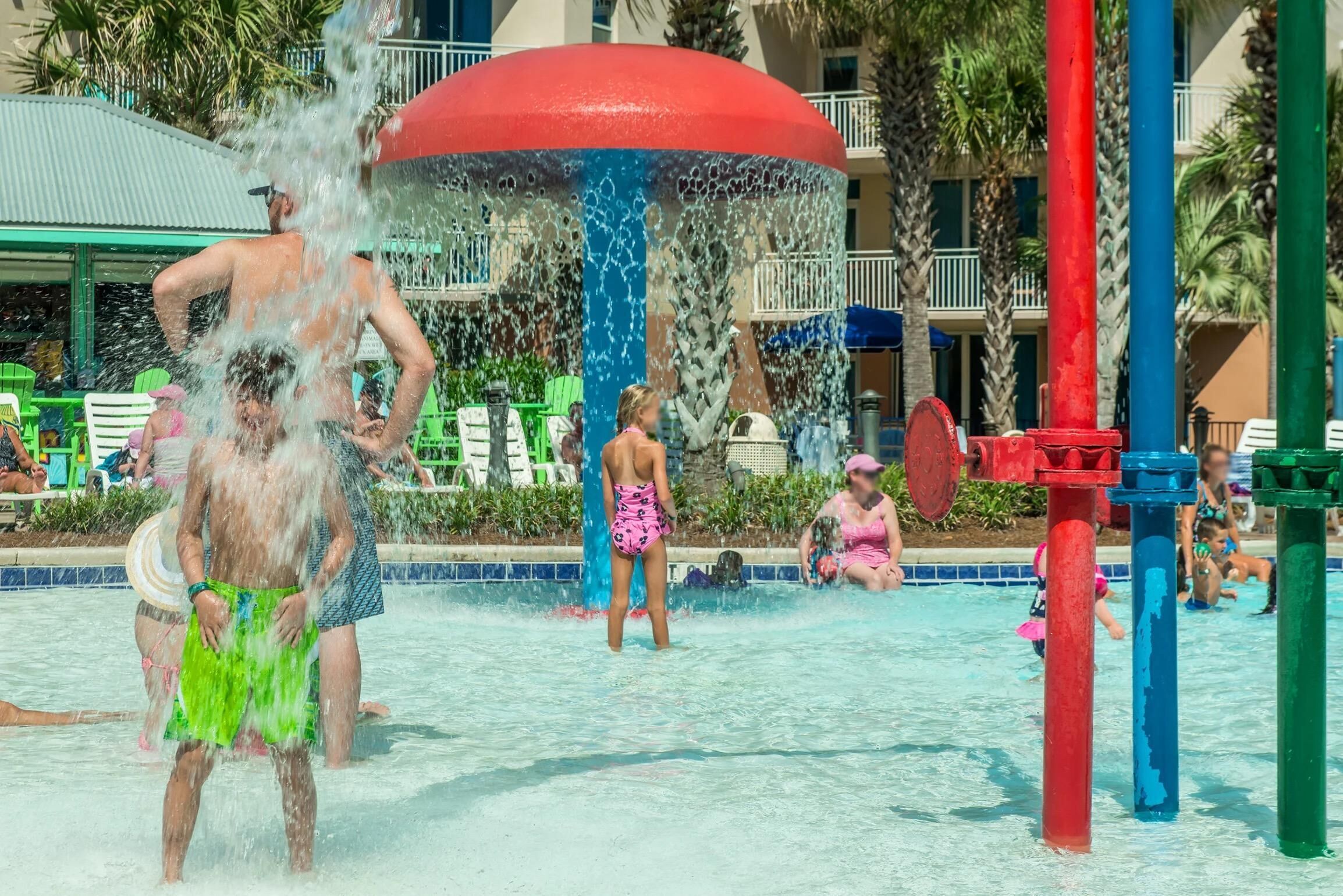 A water park with a large water fountain, pool, and lounge area with chairs.