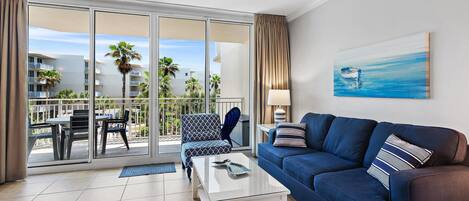 Una sala de estar moderna con un sofá azul, una mesa de centro de vidrio y vistas a un balcón con mobiliario exterior.