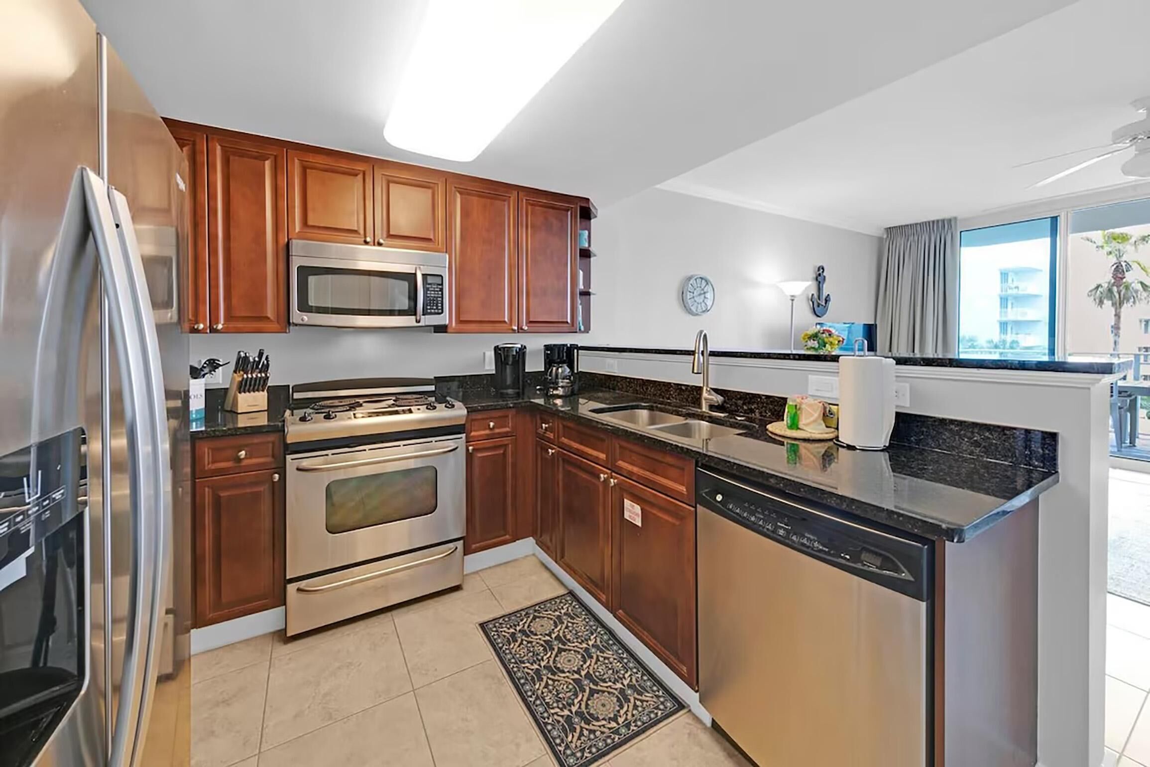 A modern kitchen with stainless steel appliances, wooden cabinets, and a large window providing a view of the outside.