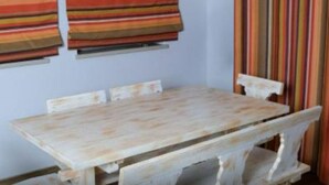 Une table en bois rustique, accompagnée d’un banc, de rideaux à rayures et d’un store à rayures.