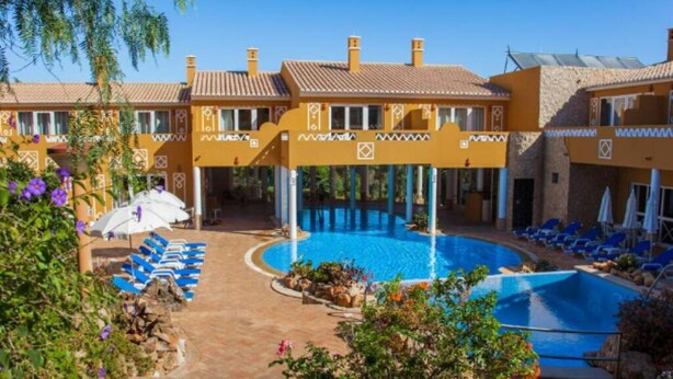 Un hôtel doté d’une piscine, de chaises longues et d’un espace abrité avec des parasols.