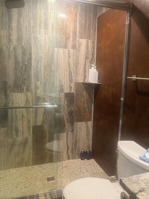 Un baño con cabina de ducha de vidrio, inodoro y zona de lavamanos con artículos de aseo.