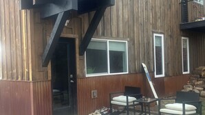 En træbygning med en overdækket terrasse, udendørs møbler og en grussti.