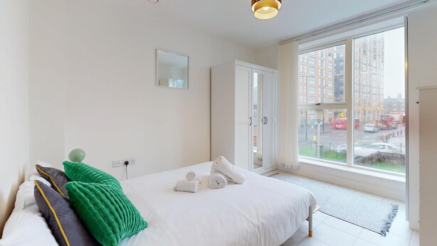 Et hotelværelse med en seng, et spejl, et vindue med udsigt til bygninger og en dør.