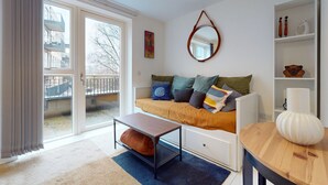 En moderne stue med sofa, sofabord, spejl og udsigt til den tilhørende balkon.