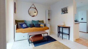 En moderne stue med sofa, lille bord, spejl og et køkken i baggrunden.
