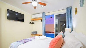 A bedroom with a bed, a ceiling fan, a TV, a window with curtains, and a balcony view. - Condo Pool Palapa Lounge Free Parking Onsite (La Paz)