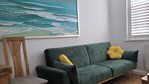 Ett rum med en grön soffa, en trästol och en stor målning som föreställer havet.
