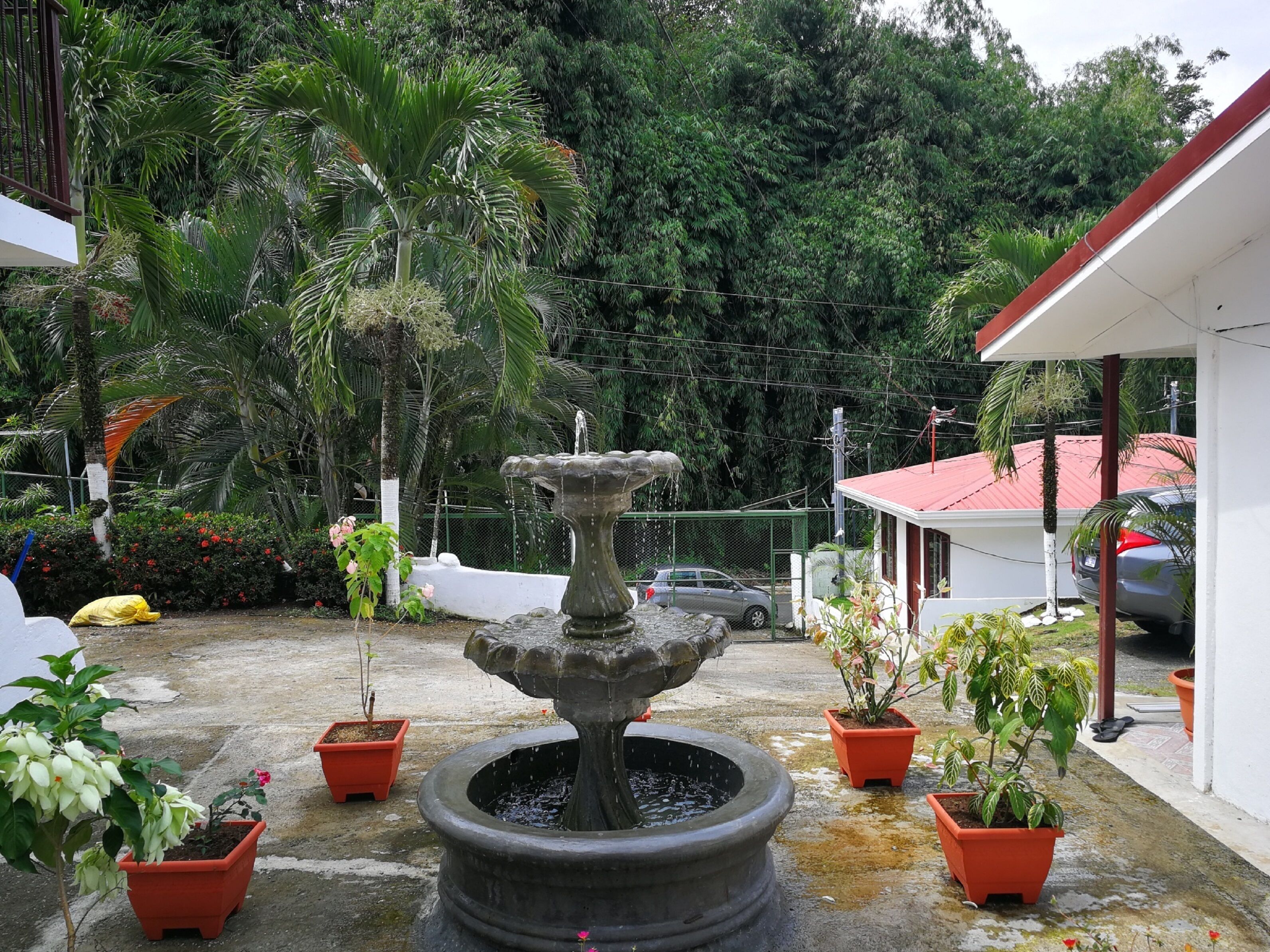 A courtyard with a central stone fountain, surrounded by potted plants and a parked car.