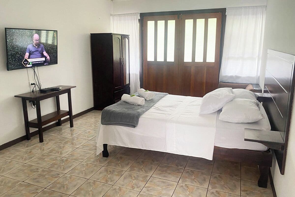 A hotel room with a bed, a television, a wardrobe, and a window with curtains.