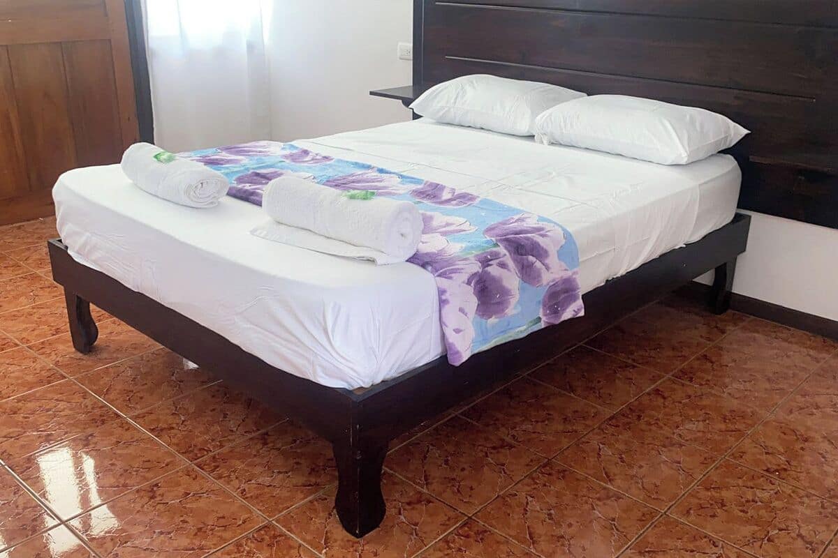 A bed with white linens, a floral-patterned blanket, and rolled towels on the side.