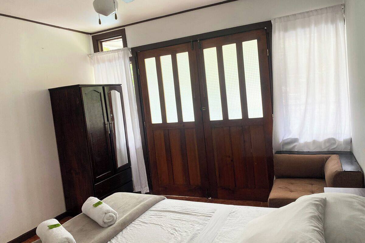 A room with a bed, a wooden wardrobe, a sofa, and a window with curtains.