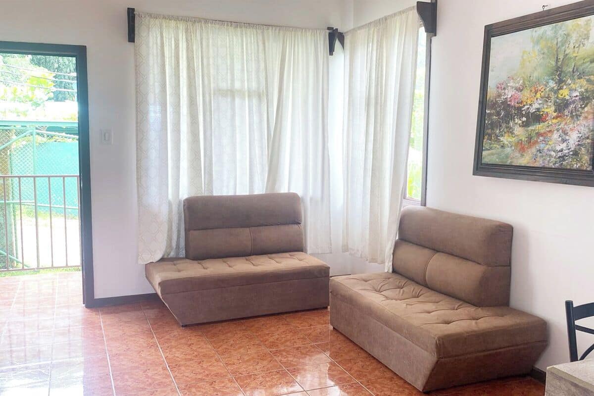 A room with a sofa, a painting, and a view of a green outdoor area.