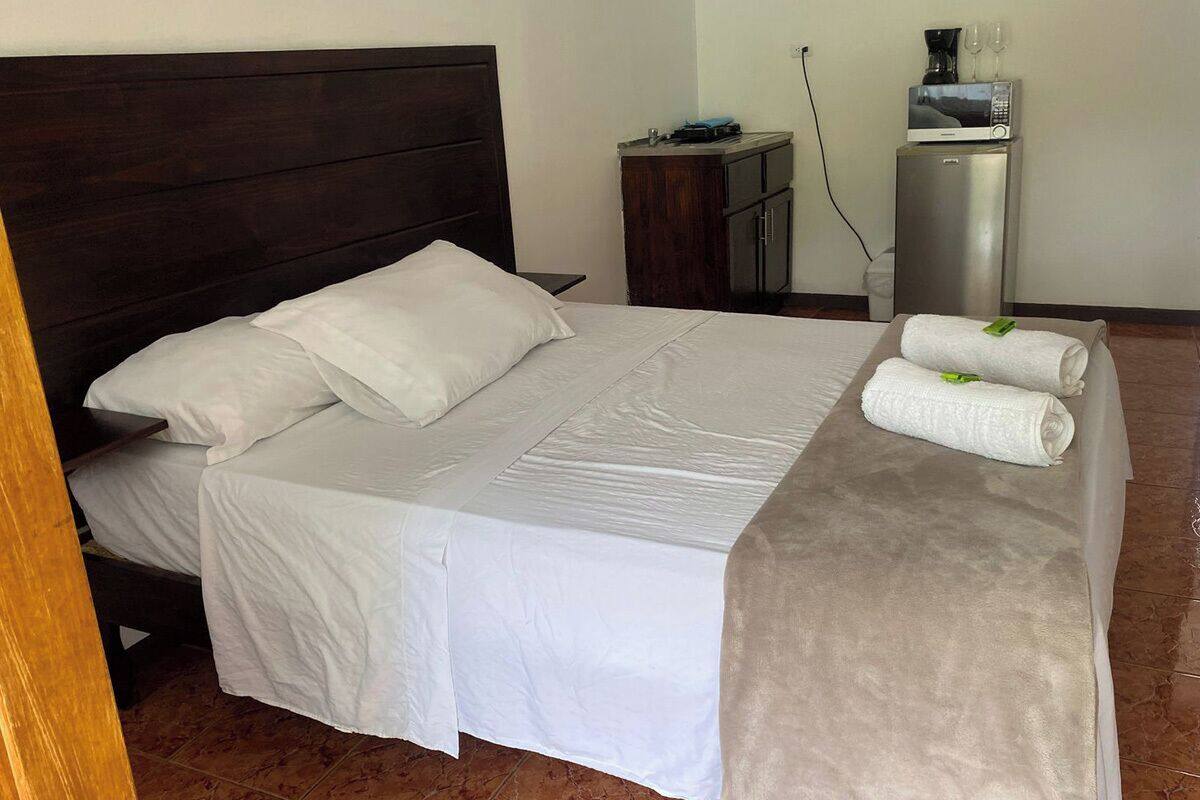 A neatly made bed with white linens, a dark headboard, and a small wooden nightstand with a lamp.