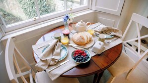 Ein Esstisch mit Teekanne, Brot, Obst und einem Blumenstrauß.