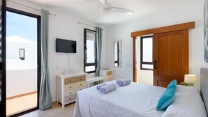 Ein Schlafzimmer mit Bett, Kommode, Fernseher, Deckenventilator und einer Schiebetür.