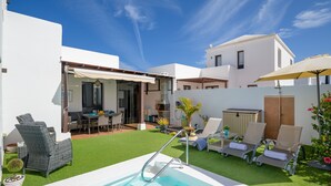 Ein moderner Poolbereich im Freien mit Kunstgrasanlage, Liegestühlen und einer überdachten Terrasse.