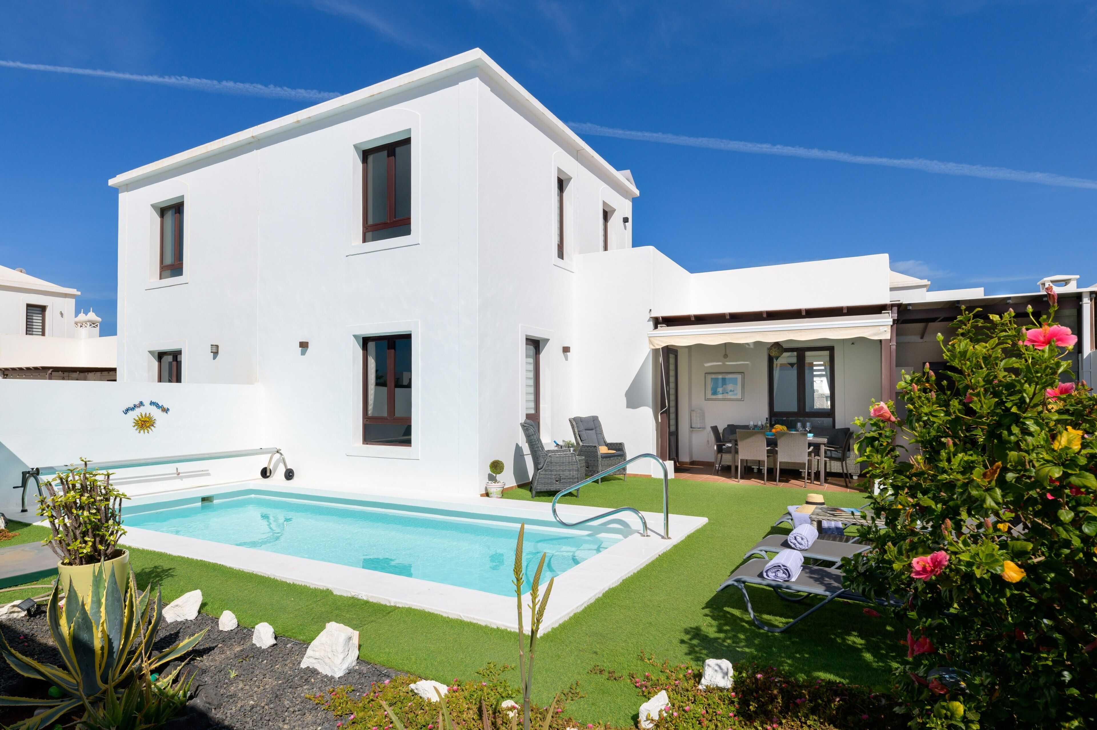 A modern two-story building with a swimming pool, outdoor seating, and a well-maintained garden.