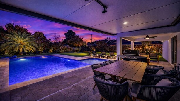 Un espace extérieur avec une piscine, une table et des chaises, un barbecue et une vue sur le coucher de soleil.