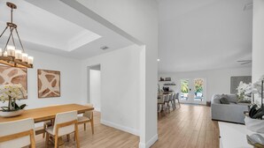 Un vaste espace de vie comprenant une table à manger en bois, des chaises blanches et un canapé gris.