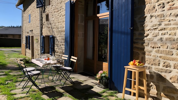 A stone building with a wooden table and chairs outside, a wooden stool with fruit, and a flower pot. - Guest Rooms “La Grande & La Jumelle” with Shared Terrace, Garden, and Wi-Fi (Soubrebost)