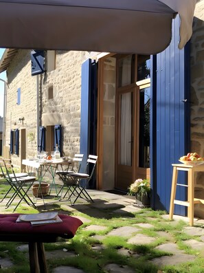Un área de comedor al aire libre con una mesa dispuesta para dos personas, una cesta de mimbre y un cojín rojo.