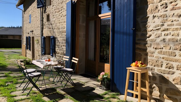 A stone building with a wooden table and chairs outside, a wooden stool with fruit, and a flower pot.