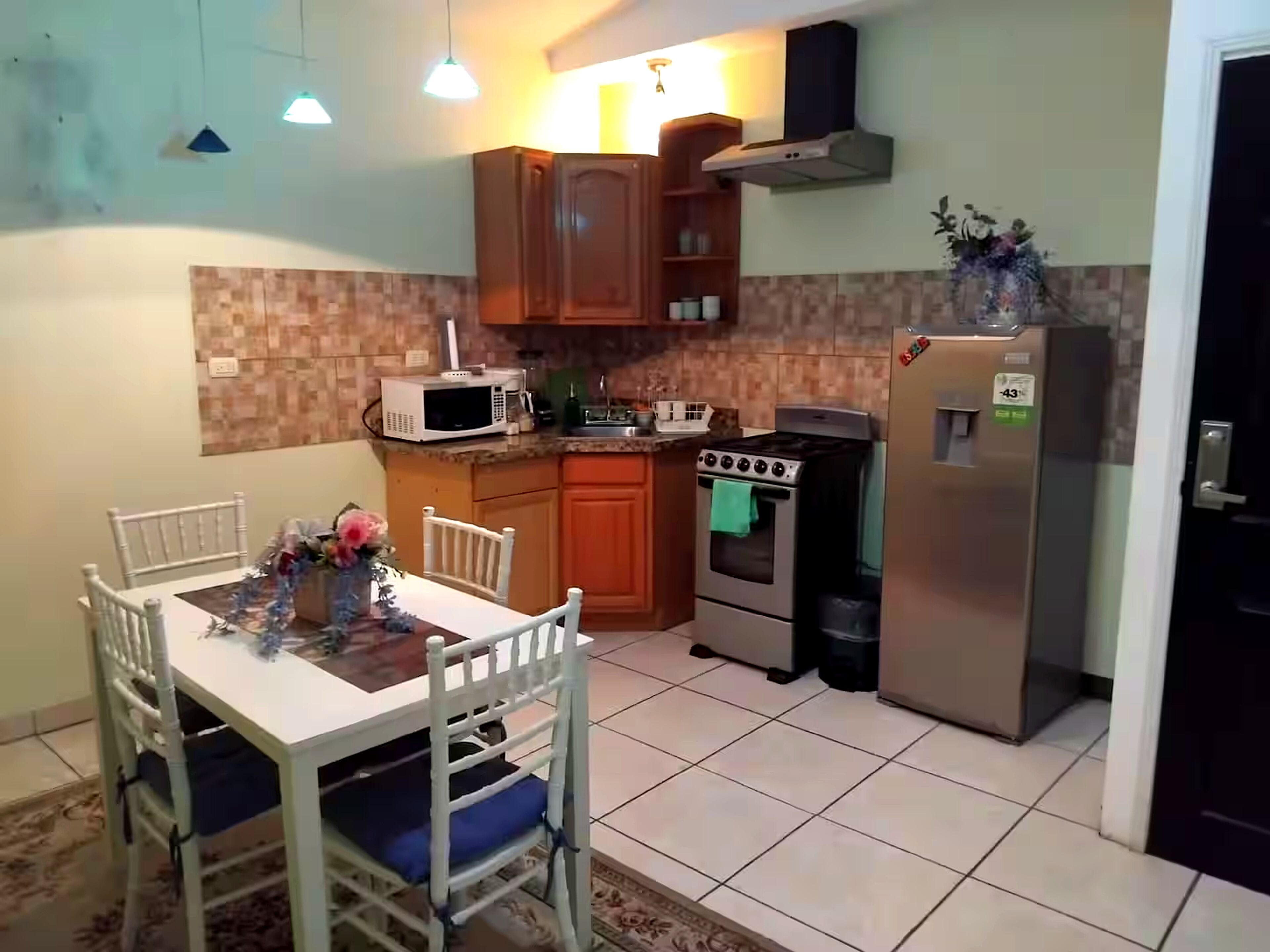 Cocina compacta con una mesa, sillas, microondas, estufa y refrigerador.