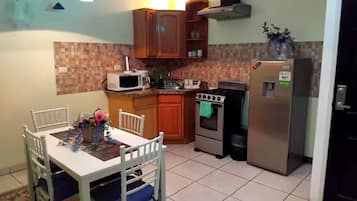 Cocina compacta con una mesa, sillas, microondas, estufa y refrigerador.