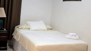 Un dormitorio ordenado con una cama, una mesita de noche, una lámpara, un cuadro en la pared y una silla.