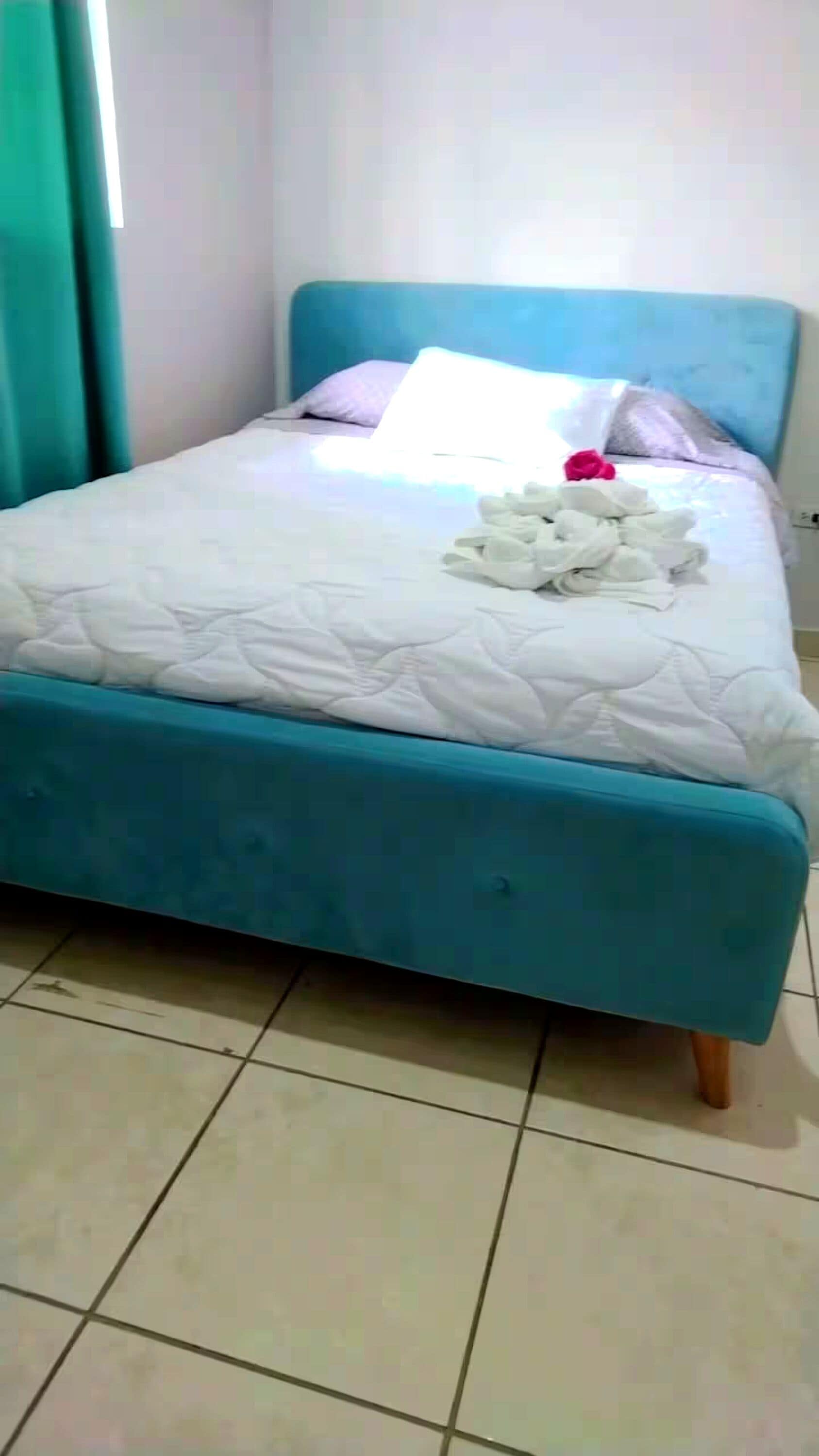 A bed with a teal headboard, white bedding, and a pile of white towels.
