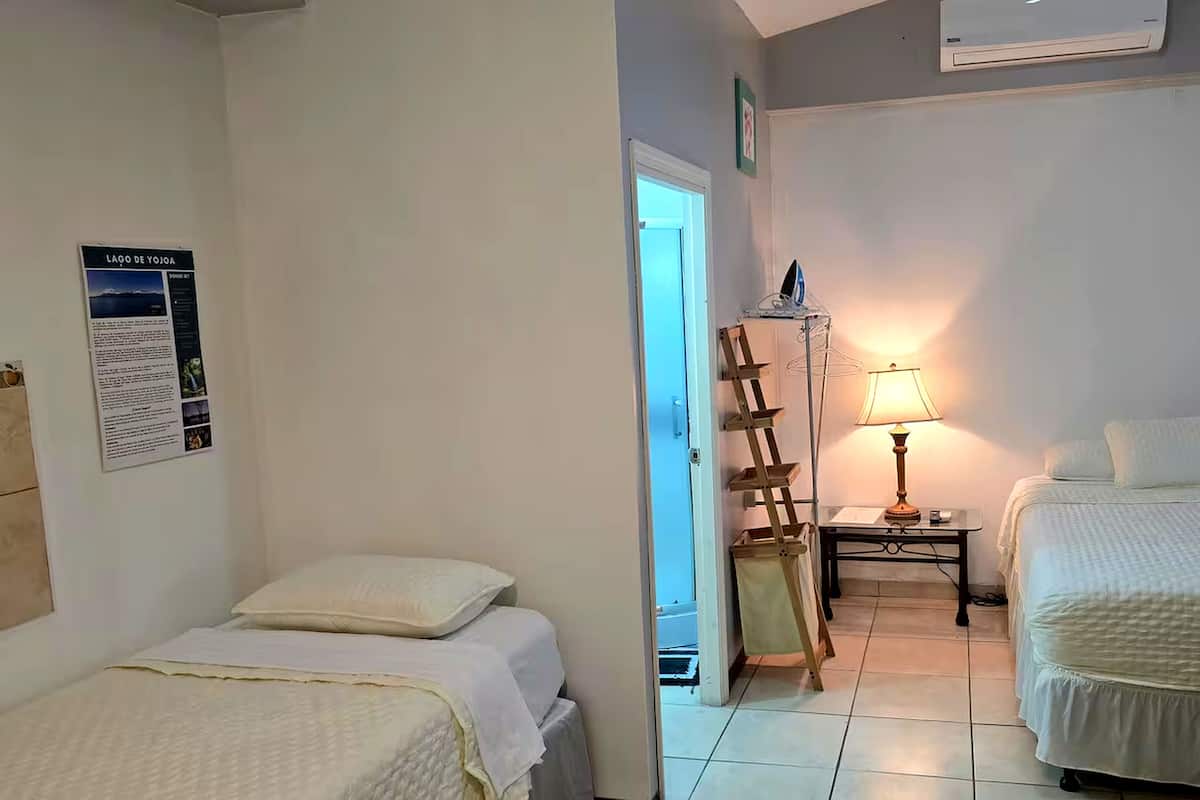 Een hotelkamer met twee bedden, een houten trap, een tafel met een lamp en een poster aan de muur.