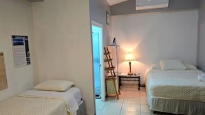 A hotel room with two beds, a wooden ladder, a table with a lamp, and a poster on the wall.
