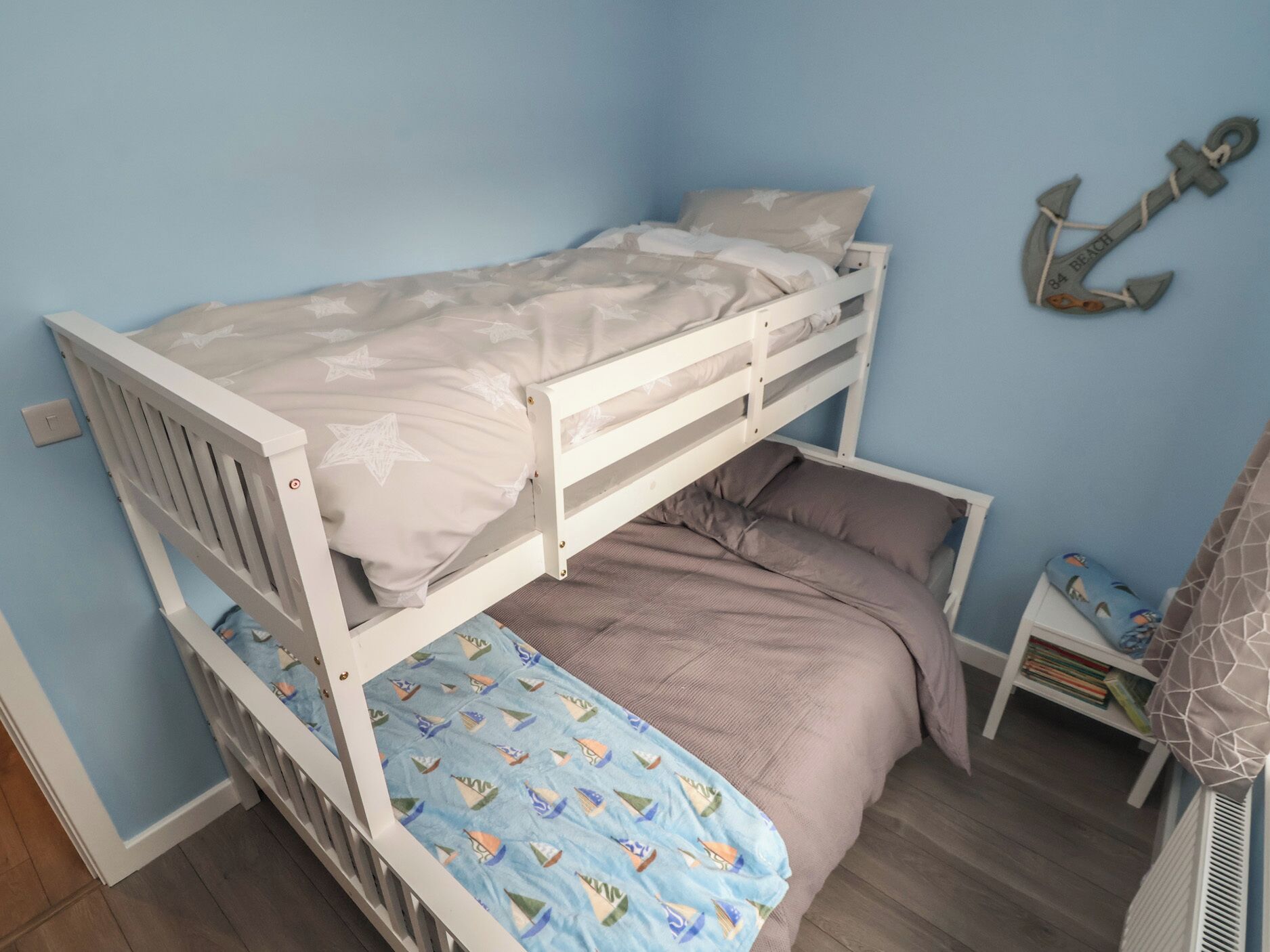 Una cama litera con una cama inferior, una mesita de noche pequeña con un libro, y una decoración de ancla montada en la pared.