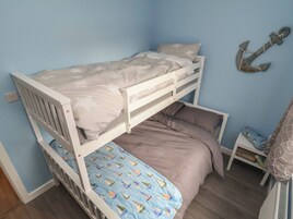 Una cama litera con una cama inferior, una mesita de noche pequeña con un libro, y una decoración de ancla montada en la pared.
