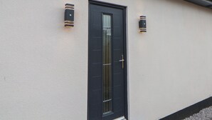 A building with a dark door, light-colored walls, and two wall-mounted light fixtures. - Mikes Place On The Cove (Rhyl)