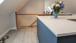 A modern kitchen with a wooden staircase, a white countertop, and a vase with flowers. - Mikes Place On The Cove (Rhyl)