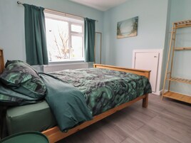 A bedroom with a bed, a window with curtains, a radiator, a door, and a painting on the wall.