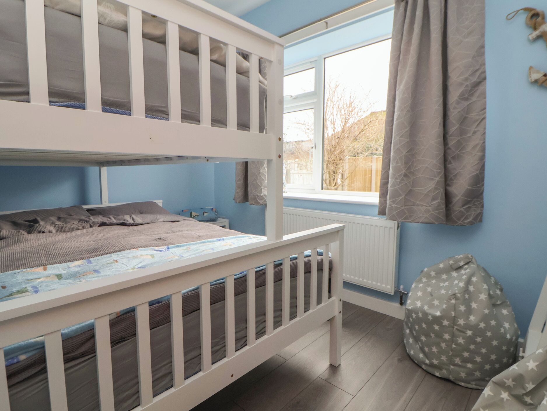 Une chambre pour enfant avec un lit superposé, une fenêtre, un radiateur et un pouf en forme d’étoile.