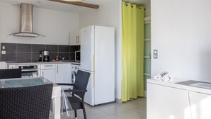 A modern kitchen with a refrigerator, washing machine, and dining area with a glass table and chairs. - T2 Vert Anis Apartment with Wi-Fi (Salies-de-Béarn)