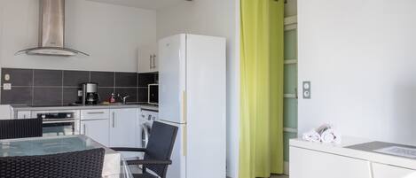 A modern kitchen with a refrigerator, washing machine, and dining area with a glass table and chairs.