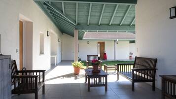 A covered patio area with wooden furniture, potted plants, and a view of a building in the background.